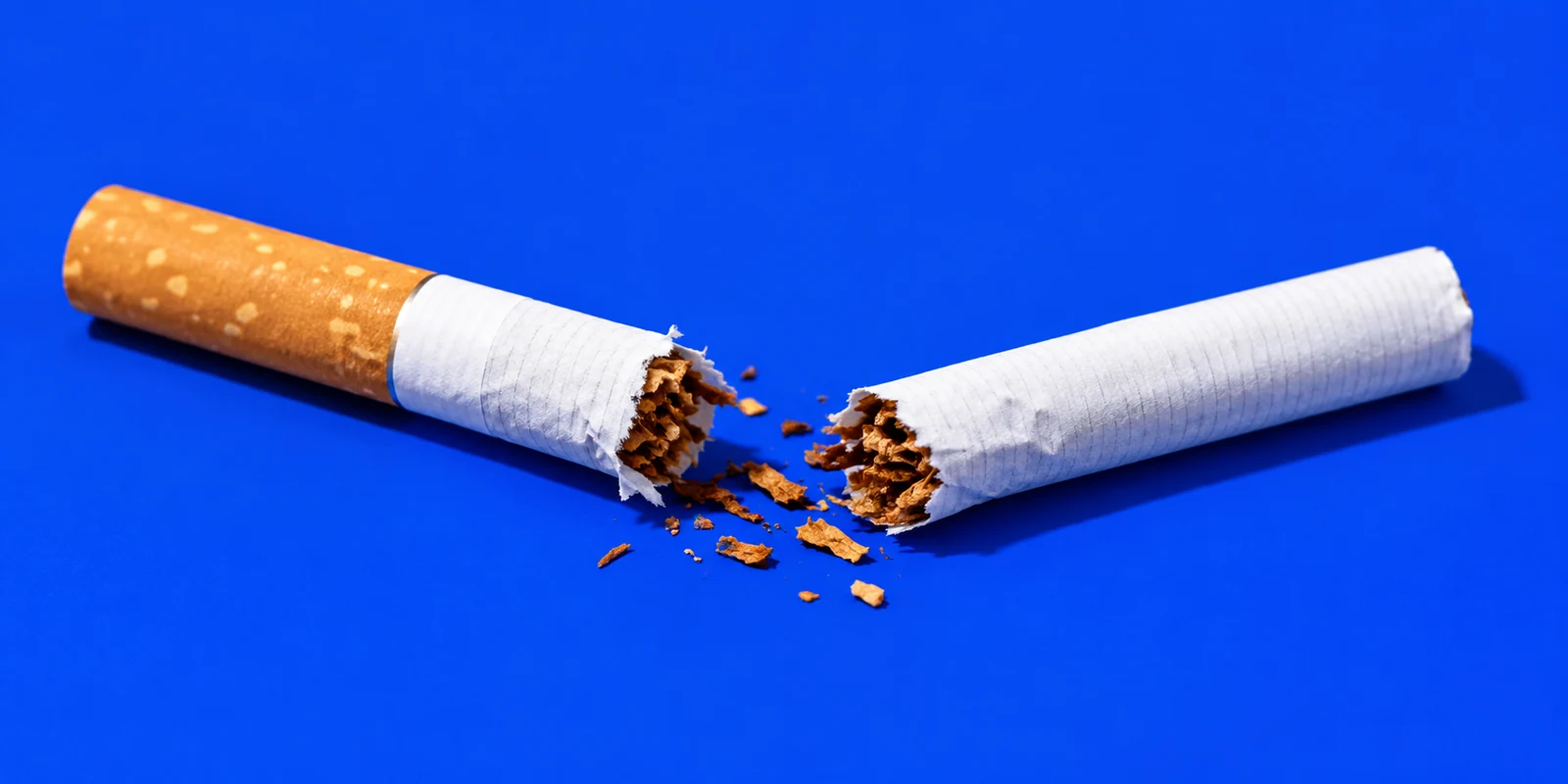 A cigarette broken in two against a bright blue background.
